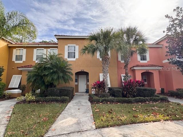 A two-story townhouse with tan and pink stucco exteriors, palm trees, and a concrete walkway — 4778 VERO BEACH PLACE, KISSIMMEE, FL