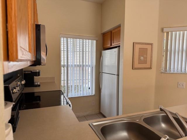 A kitchen features light-colored countertops, a double sink, wood cabinets, and a white refrigerator — 4778 VERO BEACH PLACE, KISSIMMEE, FL