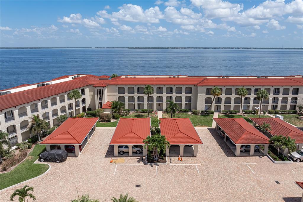 An aerial view of a waterfront apartment complex with red-tiled roofs and covered parking — 1 COLONY POINT DRIVE UNIT 15B, PUNTA GORDA, FL