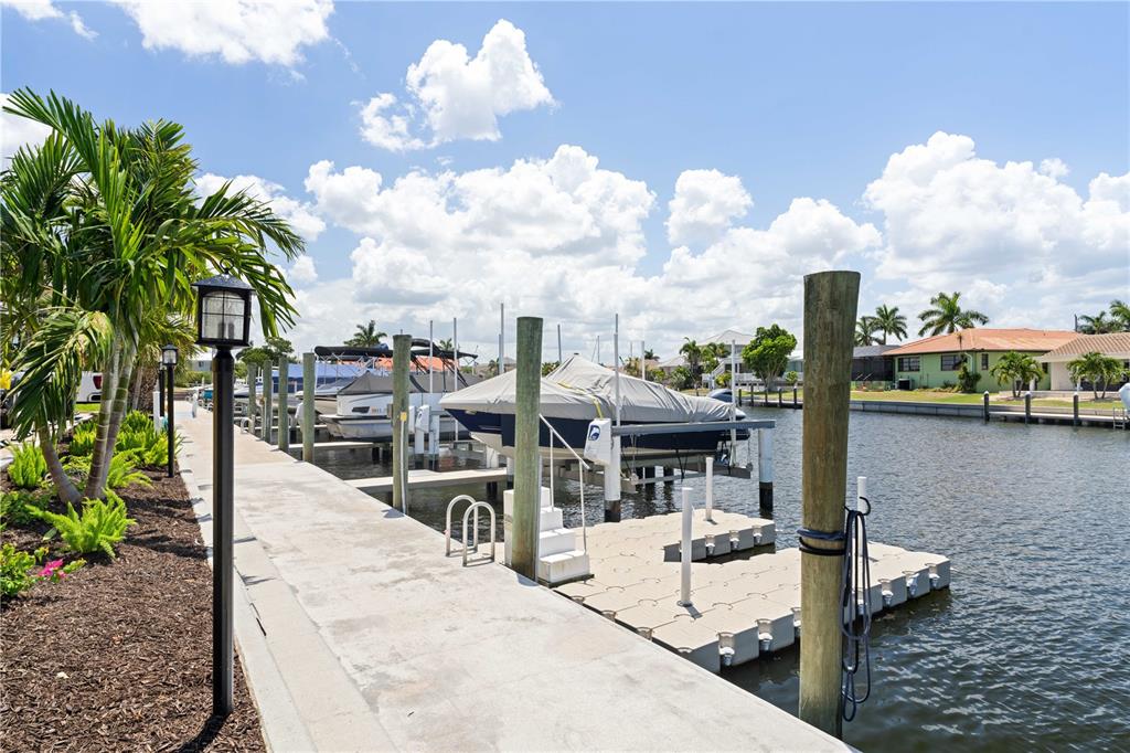 A concrete dock with a boat lift and floating platform sits along a canal — 1 COLONY POINT DRIVE UNIT 15B, PUNTA GORDA, FL