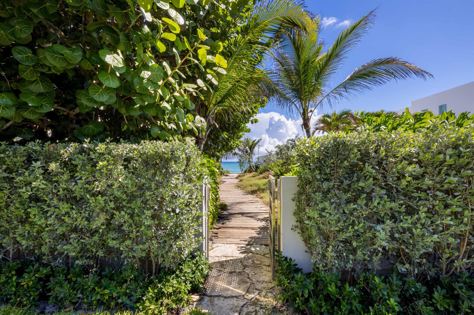 A wooden boardwalk leads through a lush garden toward the ocean under a blue sky — 1048 S Ocean Boulevard, Palm Beach FL 33480, PALM BEACH, FL