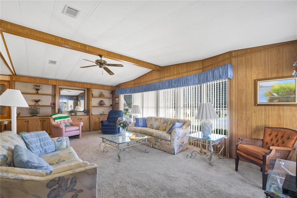 A living room features wood-paneled walls, a vaulted ceiling, floral sofas, and large windows — 4969 FOXWOOD LAKE DRIVE, LAKELAND, FL