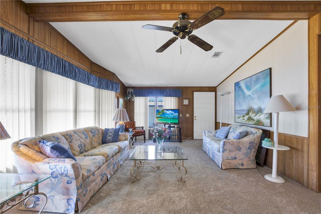 A living room features wood-paneled walls, floral sofas, a glass coffee table, and a ceiling fan — 4969 FOXWOOD LAKE DRIVE, LAKELAND, FL