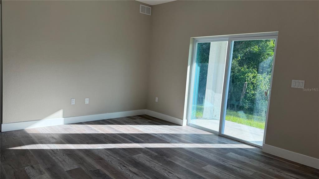 An empty room with wood-look flooring, beige walls, and a sliding glass door to outside — 11234 4TH AVENUE, PUNTA GORDA, FL