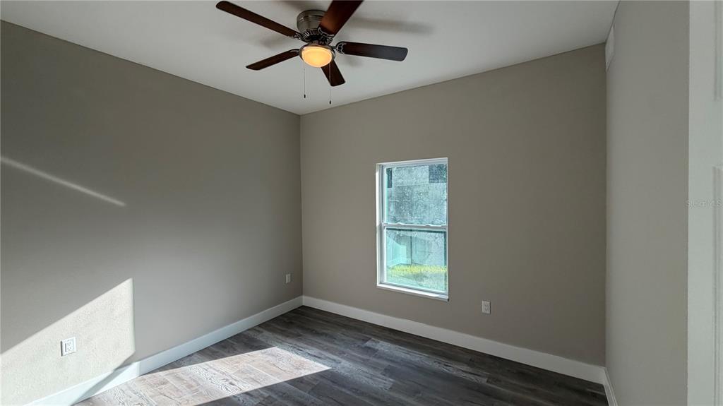 An empty bedroom features grey walls, wood-look flooring, a ceiling fan, and a single window — 11234 4TH AVENUE, PUNTA GORDA, FL