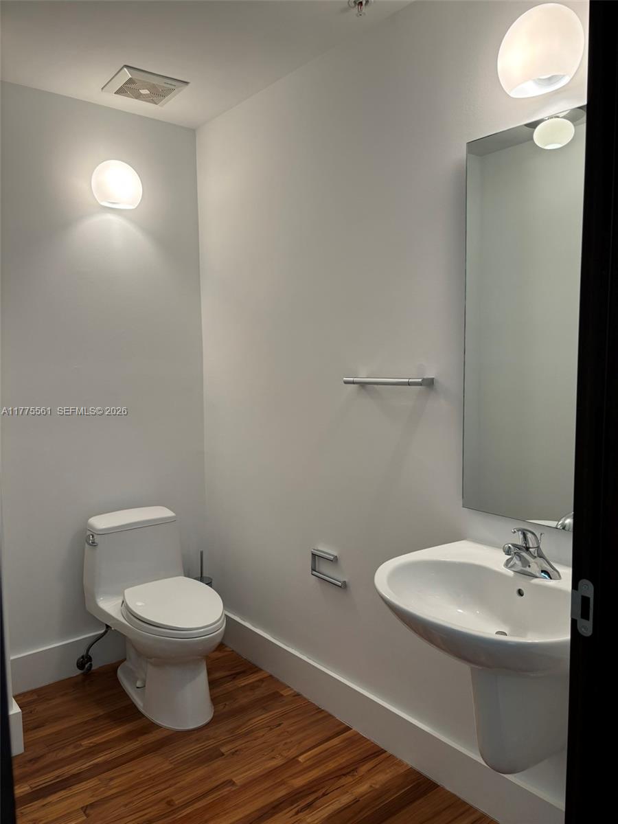 A small bathroom features a white pedestal sink, a toilet, and wood-look flooring — 2001 Meridian Ave # 309, Miami Beach FL 33139, MIAMI BEACH, FL