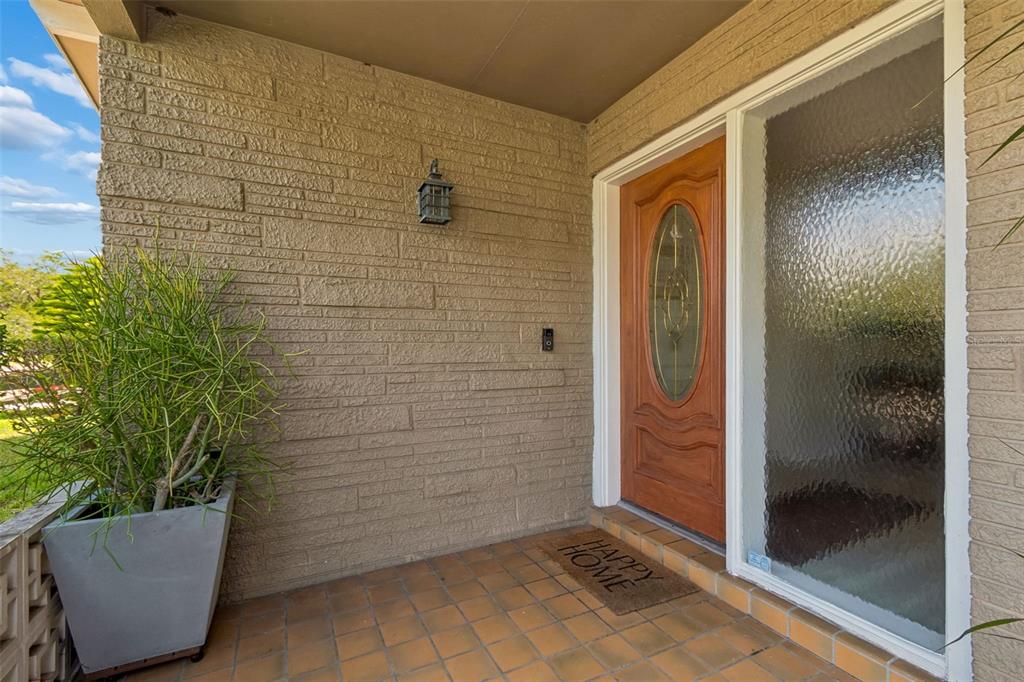 A front porch features a textured brick wall, a wooden door, and a potted plant — 546 GERSHWIN DRIVE, LARGO, FL