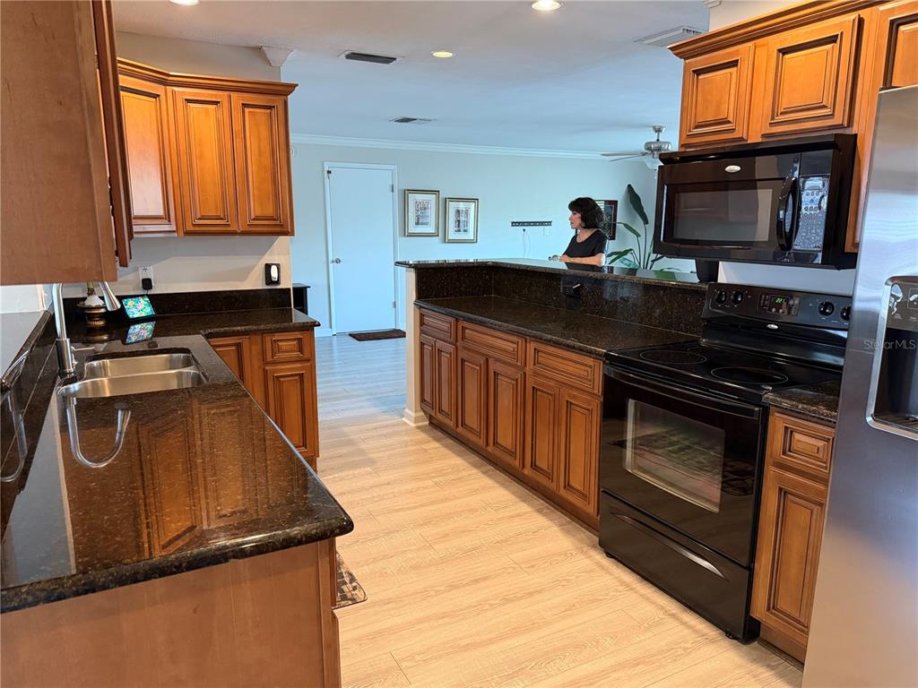 A kitchen features dark granite countertops, wood cabinets, and black appliances with light wood-look flooring — 546 GERSHWIN DRIVE, LARGO, FL