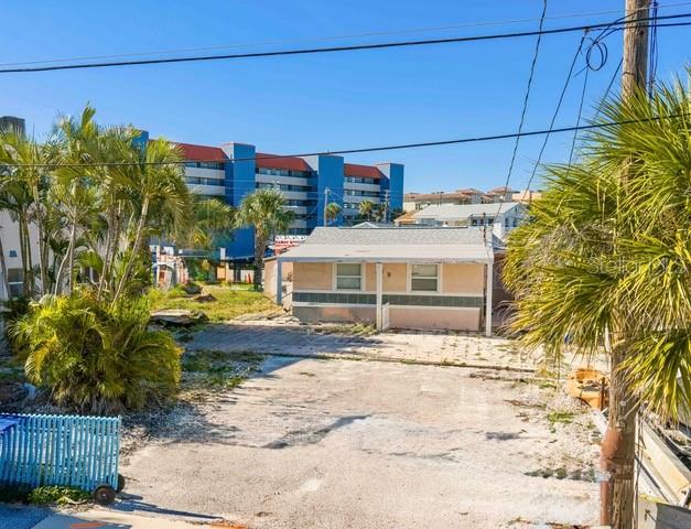 A small, single-story house sits behind a gravel lot with palm trees and a blue building — 50 137TH AVENUE CIRCLE, MADEIRA BEACH, FL