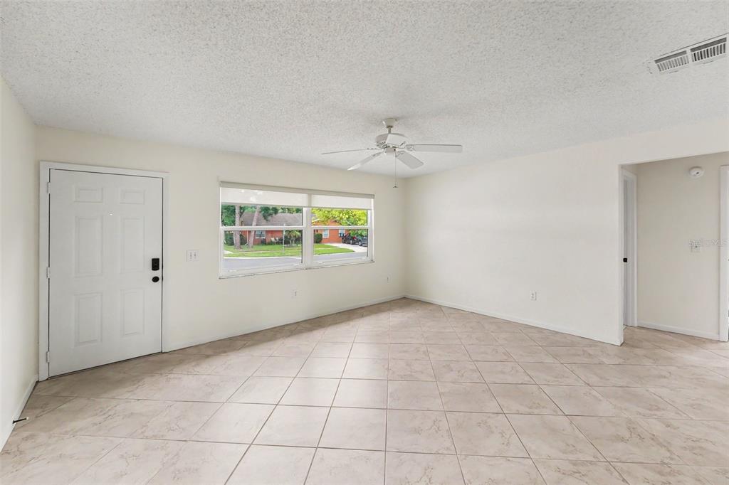 An empty room with light-colored tile flooring, a ceiling fan, and a white front door — 1836 DIANE DRIVE, CLEARWATER, FL