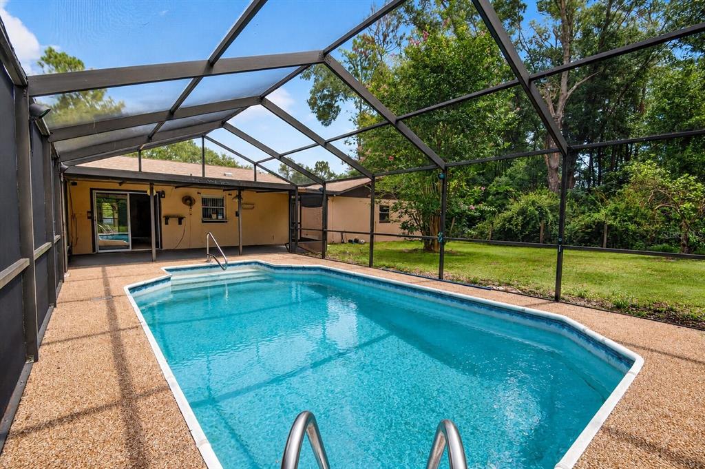 A swimming pool sits inside a screened-in patio enclosure next to a house — 5080 E PRENTICE LANE, INVERNESS, FL