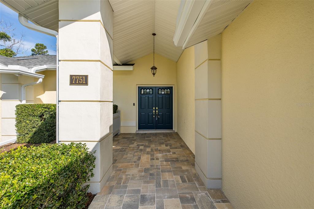 A covered entryway features a paved floor, a dark blue double door, and yellow walls — 7751 LEIGHTON CIRCLE, NEW PORT RICHEY, FL