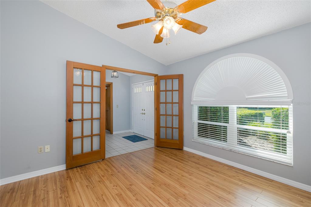 A room with wood-look flooring, French doors, a ceiling fan, and a large arched window — 7751 LEIGHTON CIRCLE, NEW PORT RICHEY, FL