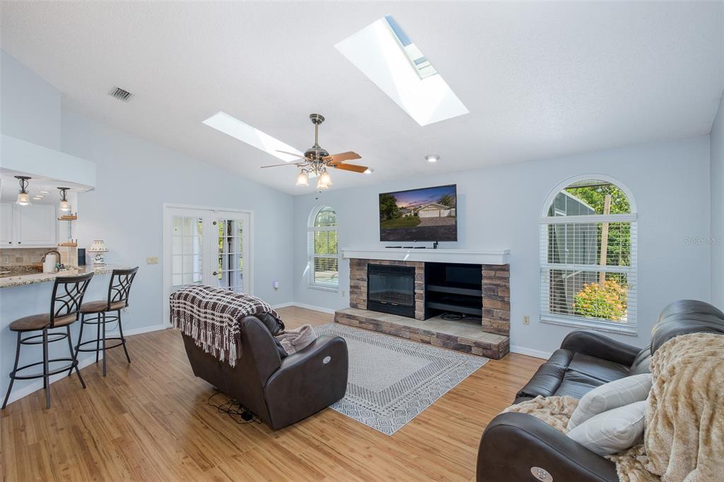 A living room with a stone fireplace, vaulted ceilings, skylights, and light wood flooring — 7751 LEIGHTON CIRCLE, NEW PORT RICHEY, FL