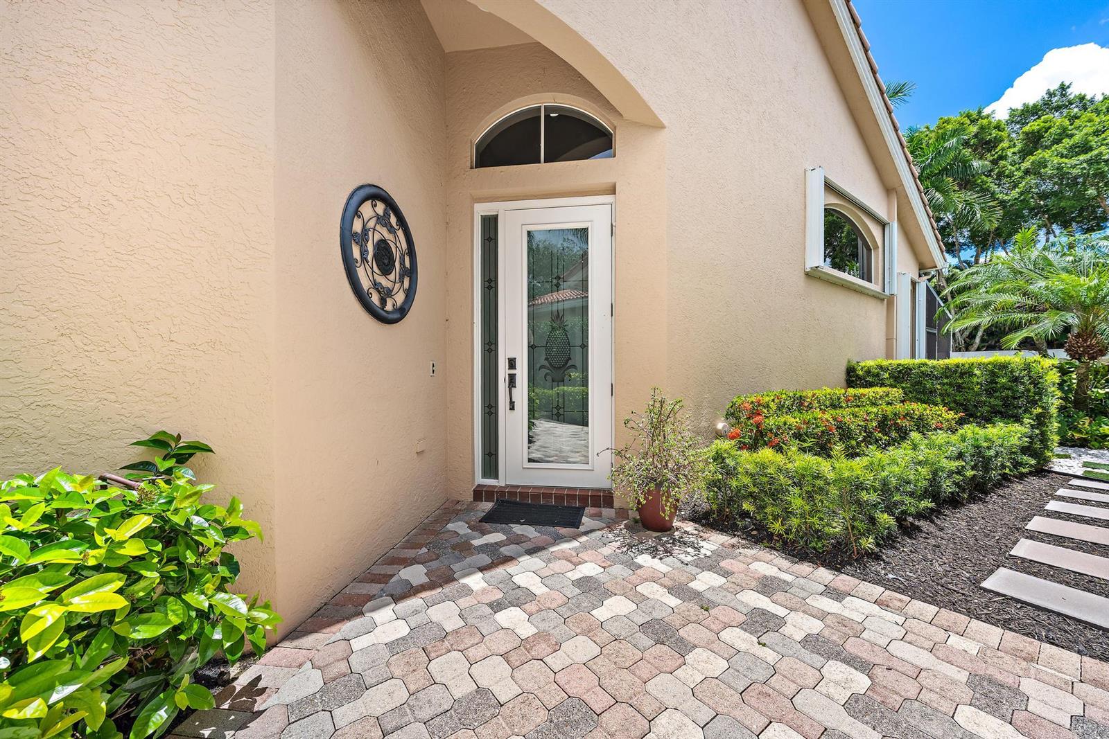 A paved walkway leads to a white front door with a pineapple design glass insert — 8164 Sandpiper Way, West Palm Beach FL 33412, WEST PALM BEACH, FL