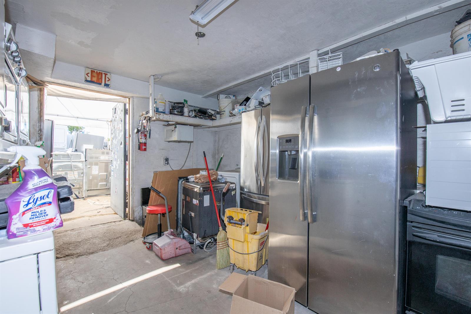 A cluttered utility room features a stainless steel refrigerator, cleaning supplies, and an open doorway — 928 S Dixie Highway, FL 33460, FL