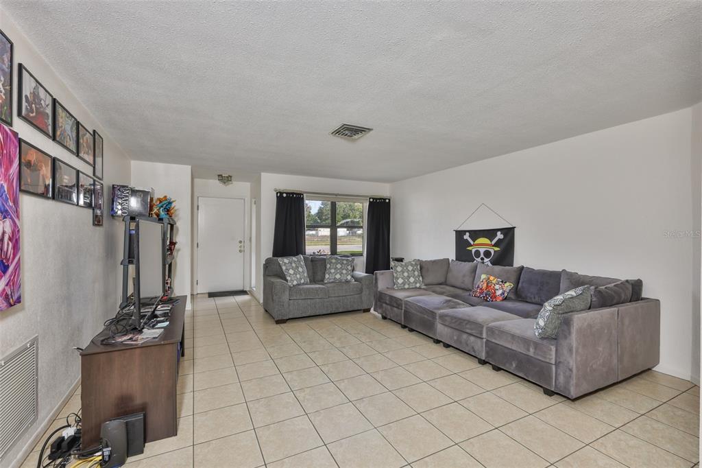 A living room features light tile flooring, a gray sectional sofa, and framed wall art — 5534 22ND AVENUE N, ST PETERSBURG, FL