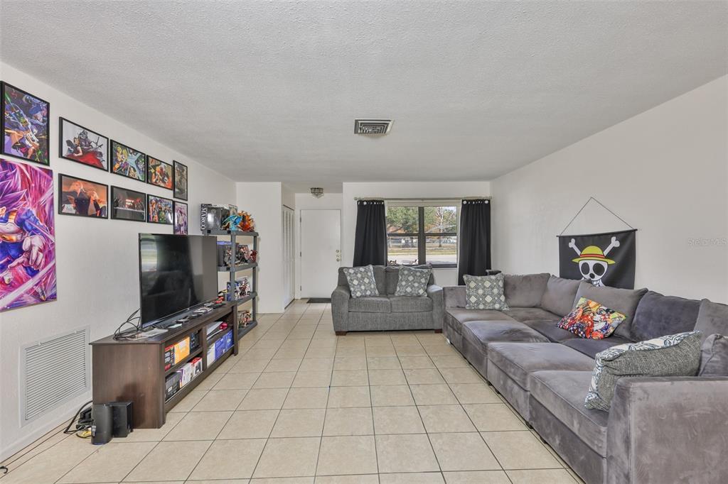A living room with tile flooring, a grey sectional sofa, and anime-themed wall decor — 5534 22ND AVENUE N, ST PETERSBURG, FL
