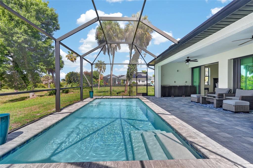 A rectangular swimming pool with steps sits inside a screened lanai with a paved patio — 592 ROTONDA CIRCLE, ROTONDA WEST, FL