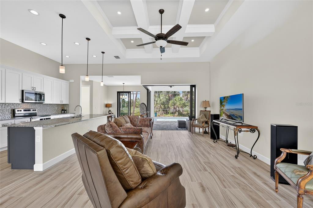 An open-concept living room and kitchen with a coffered ceiling, tile floors, and sliding doors — 592 ROTONDA CIRCLE, ROTONDA WEST, FL