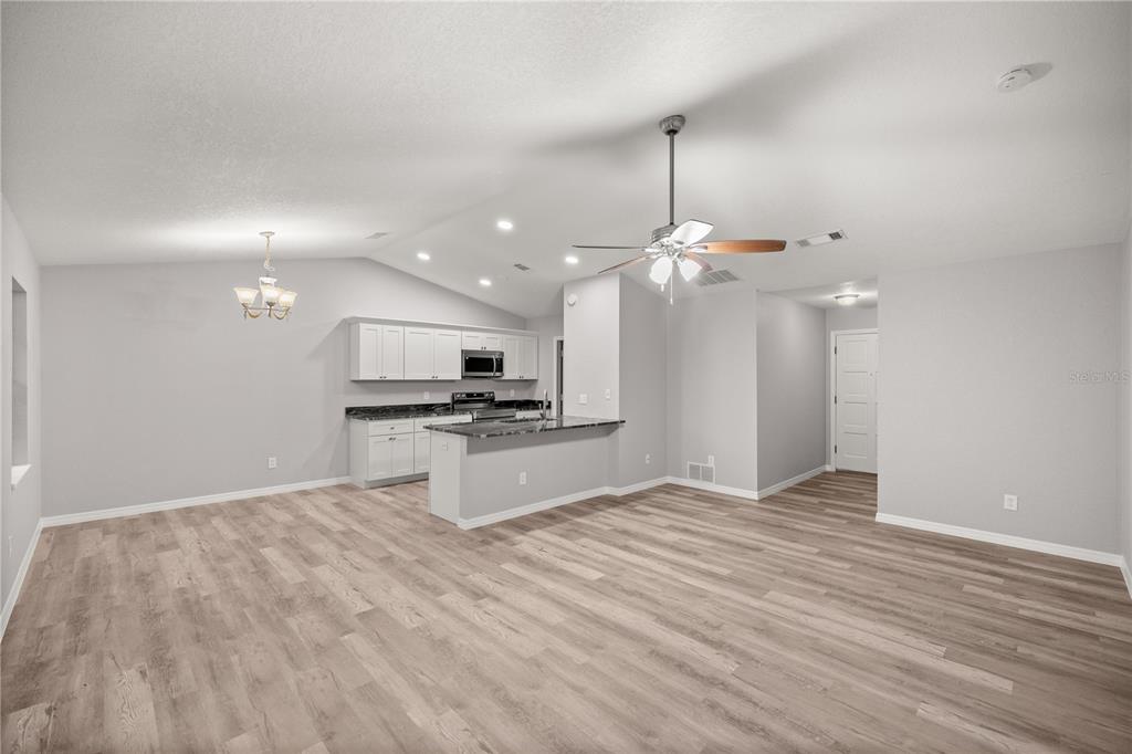 An open-concept kitchen and living area with light wood-look flooring and white cabinetry — 3730 NW 61ST PLACE, GAINESVILLE, FL