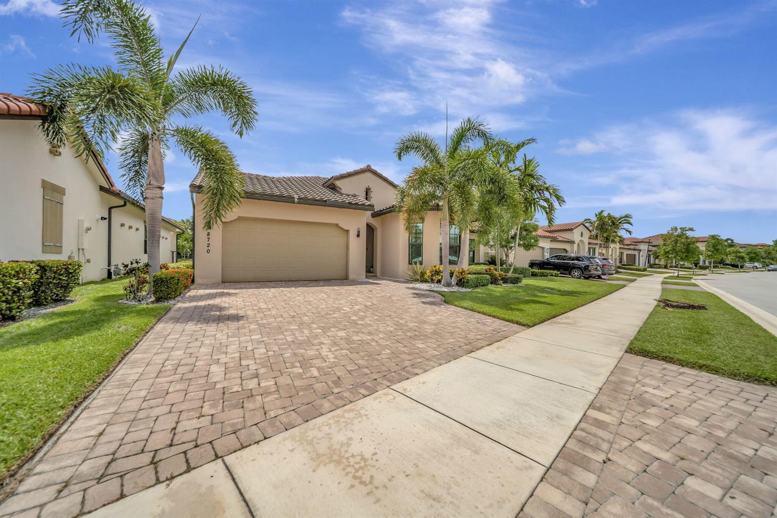 A tan single-story house with a paved driveway, palm trees, and a two-car garage — 8720 E Baypoint Circle, Parkland FL 33076, PARKLAND, FL