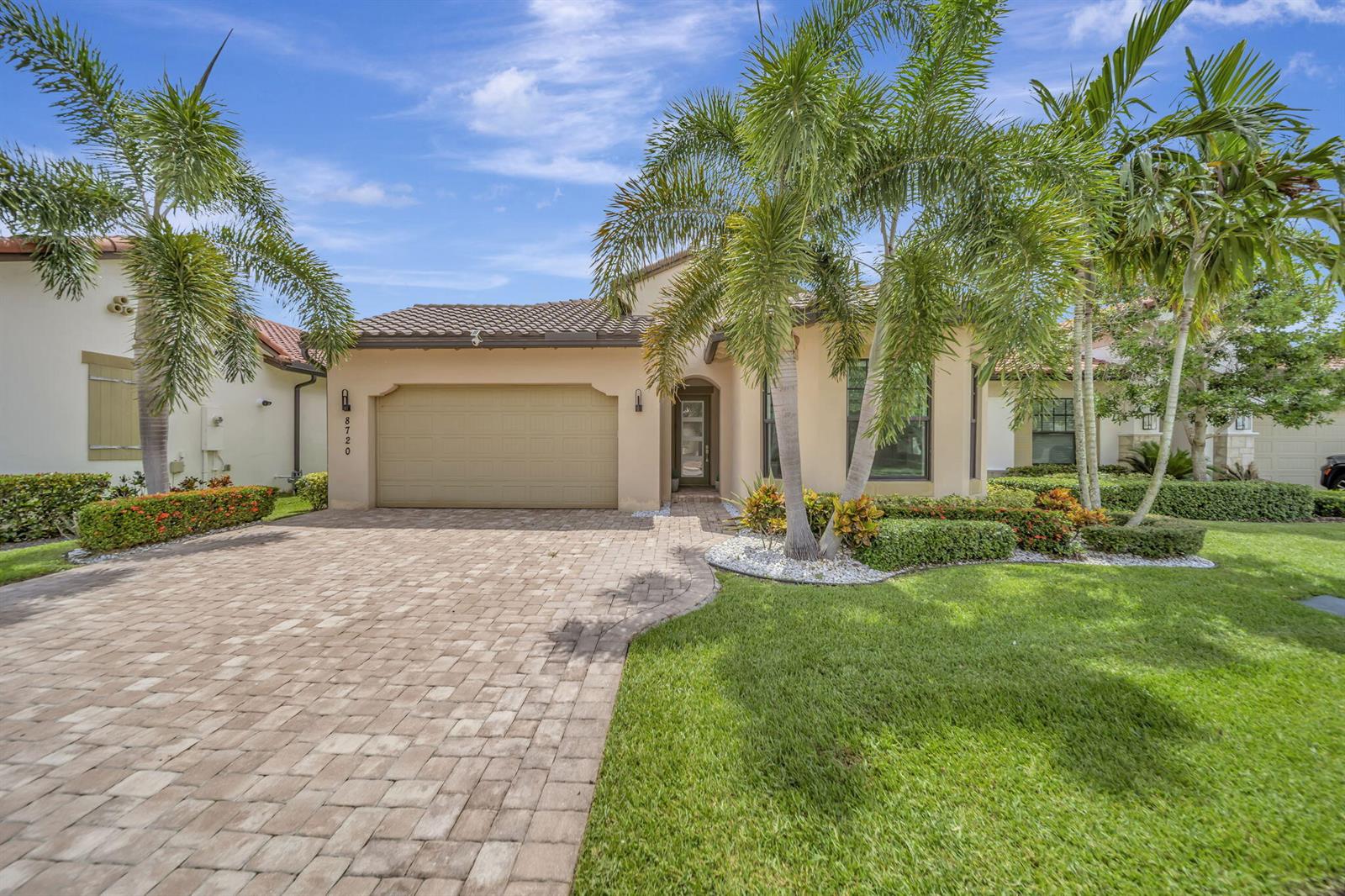 A single-story house with a beige stucco exterior, a paver driveway, and palm trees — 8720 E Baypoint Circle, Parkland FL 33076, PARKLAND, FL
