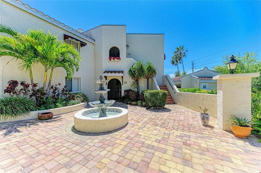 A paved courtyard features a tiered stone fountain in front of a multi-story stucco building — 6101 34TH STREET W UNIT 3D, BRADENTON, FL