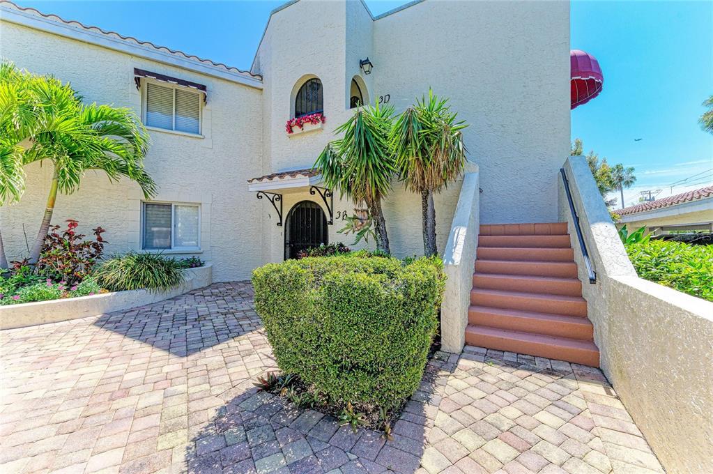 A stucco building exterior features a brick-paved walkway, a central bush, and outdoor stairs — 6101 34TH STREET W UNIT 3D, BRADENTON, FL