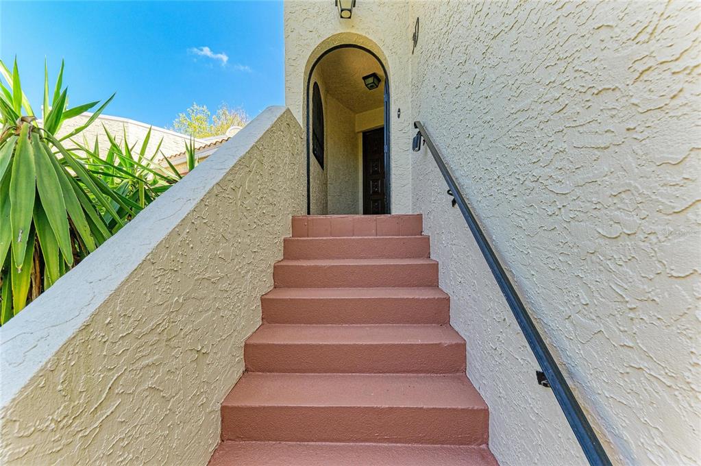 A set of red stairs leads up to an arched entryway with a dark wooden door — 6101 34TH STREET W UNIT 3D, BRADENTON, FL