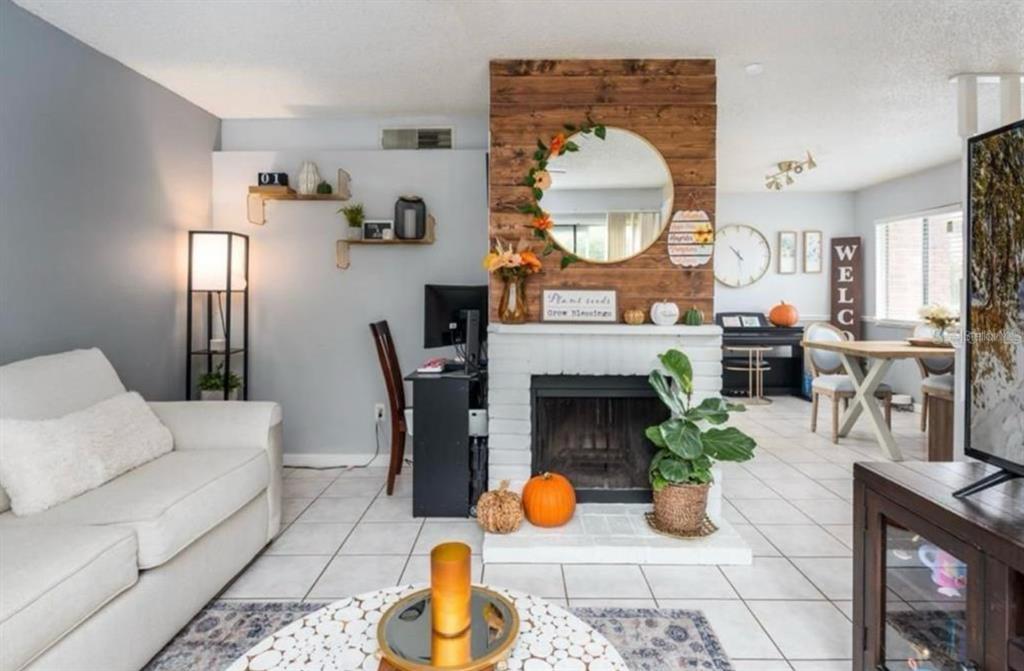 A living room features a white brick fireplace, wood-paneled accent wall, and tile flooring — 2342 HUNTINGTON GREEN COURT UNIT 2, ORLANDO, FL