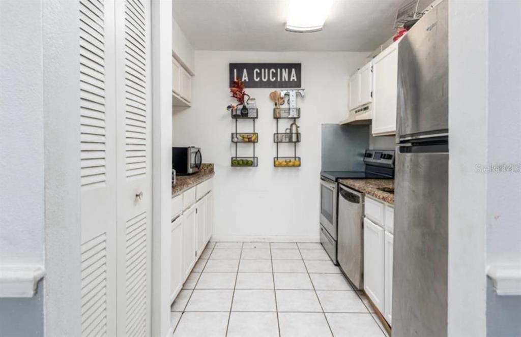 A galley-style kitchen features white cabinets, stainless steel appliances, and a tiled floor — 2342 HUNTINGTON GREEN COURT UNIT 2, ORLANDO, FL