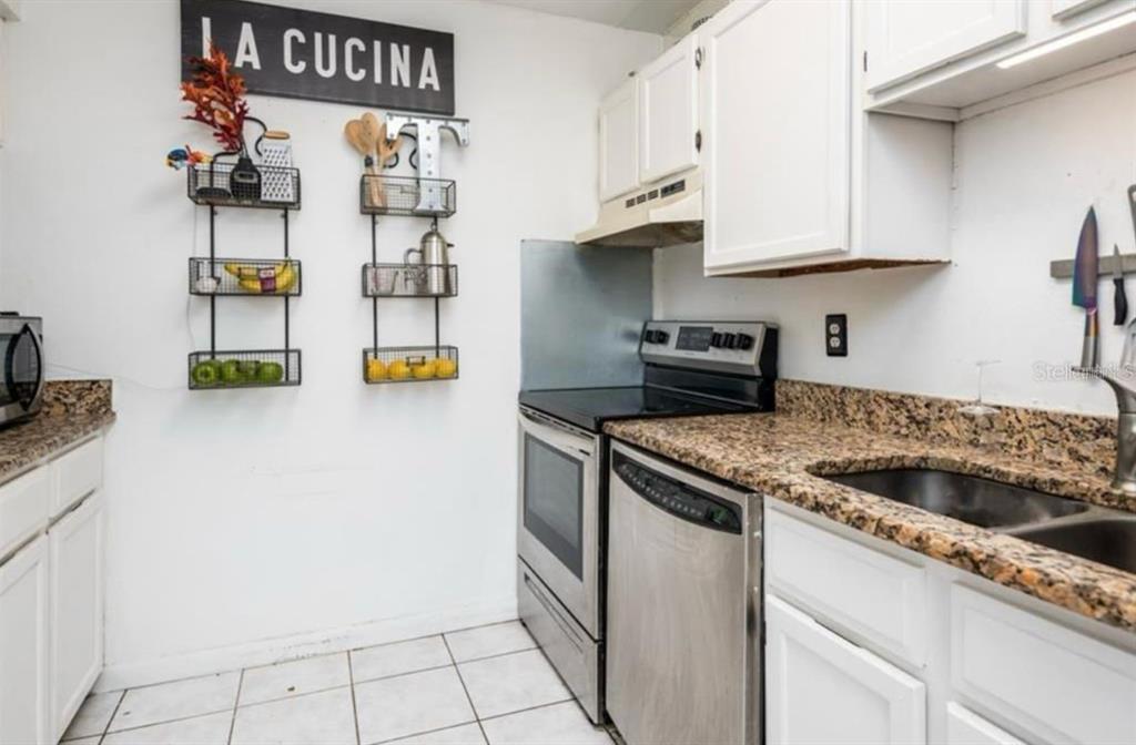 A kitchen features white cabinets, granite countertops, stainless steel appliances, and wall-mounted storage racks — 2342 HUNTINGTON GREEN COURT UNIT 2, ORLANDO, FL