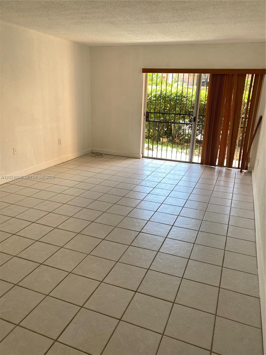 An empty room features light-colored floor tiles, white walls, and a sliding glass door — 1300 W 47th Pl # 118, Hialeah FL 33012, HIALEAH, FL