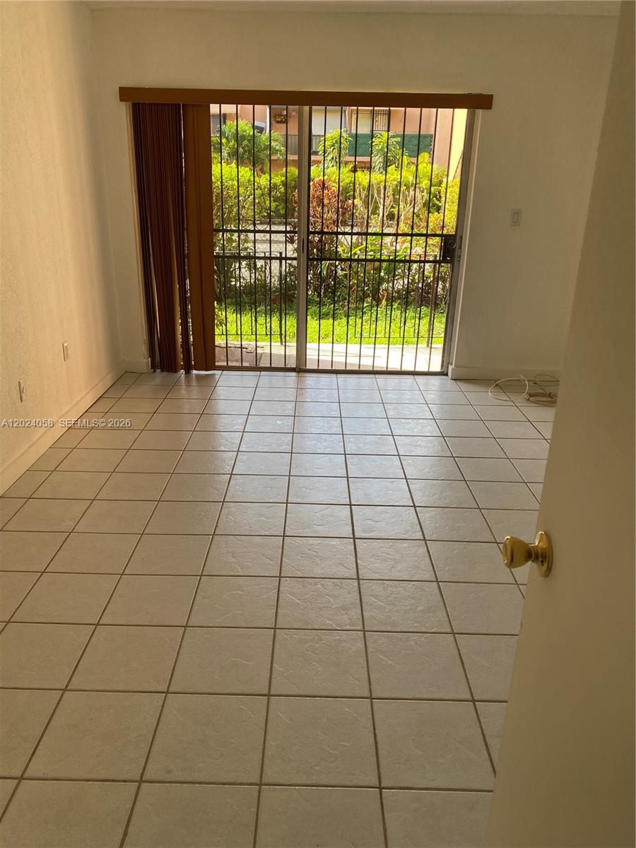A room with light-colored floor tiles, a sliding glass door, and metal security bars — 1300 W 47th Pl # 118, Hialeah FL 33012, HIALEAH, FL
