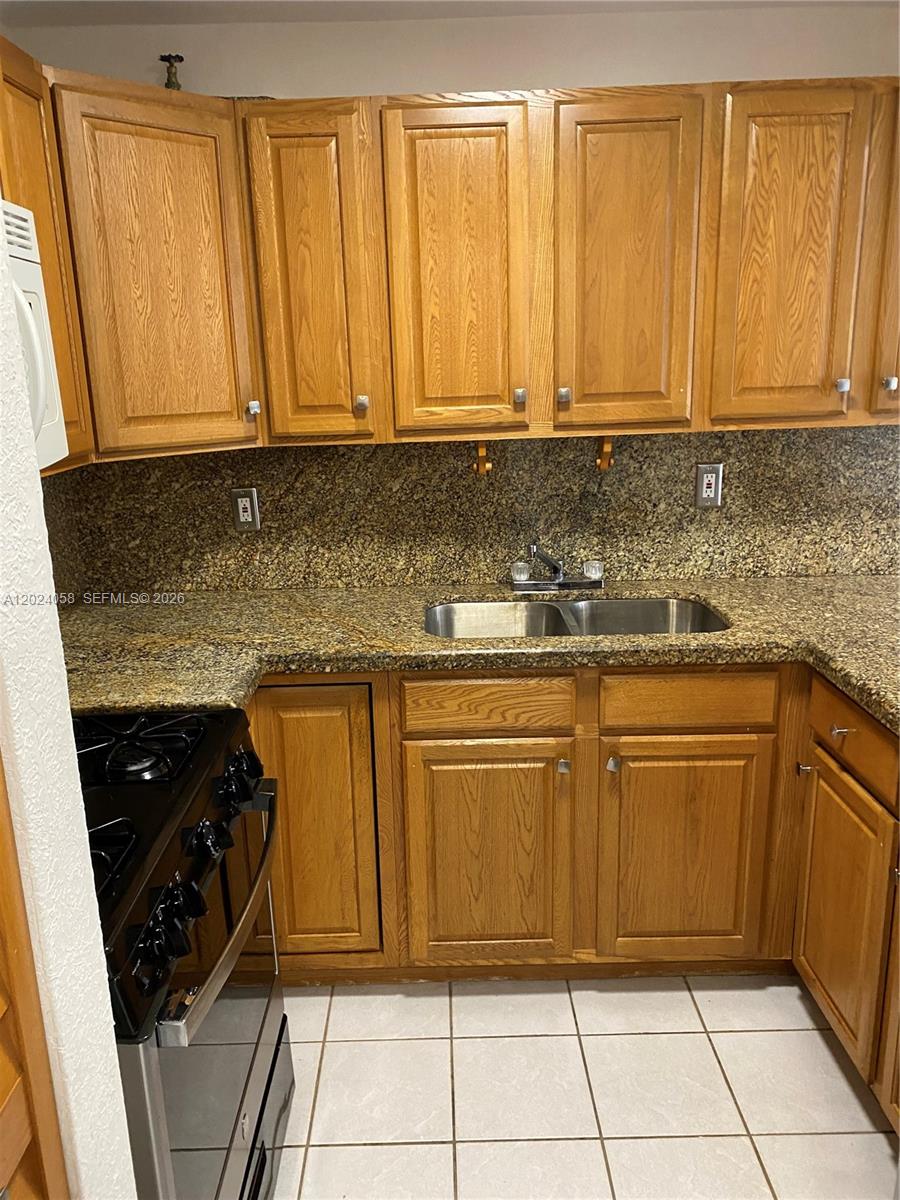A kitchen features oak cabinets, granite countertops, a double sink, and a black gas stove — 1300 W 47th Pl # 118, Hialeah FL 33012, HIALEAH, FL