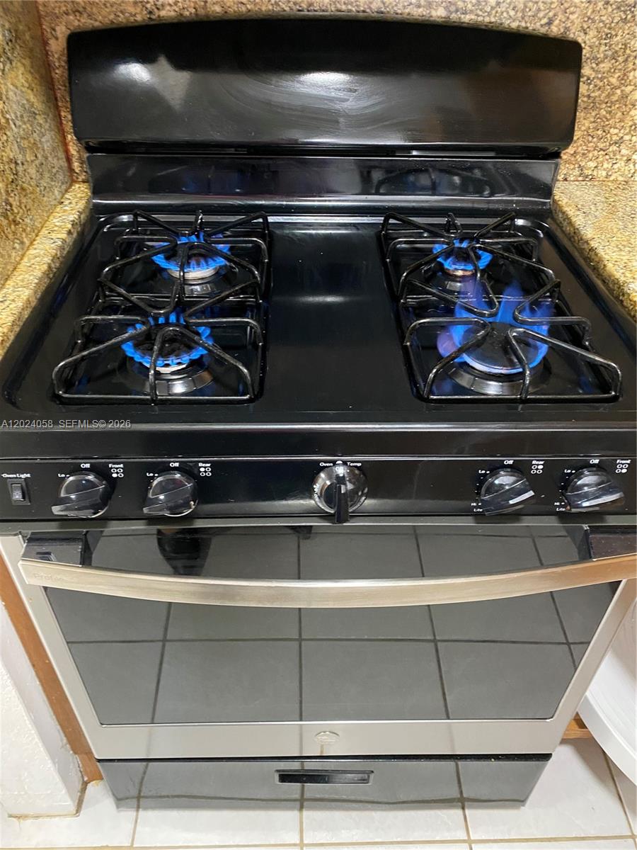 A black and stainless steel gas range is positioned between granite countertops — 1300 W 47th Pl # 118, Hialeah FL 33012, HIALEAH, FL