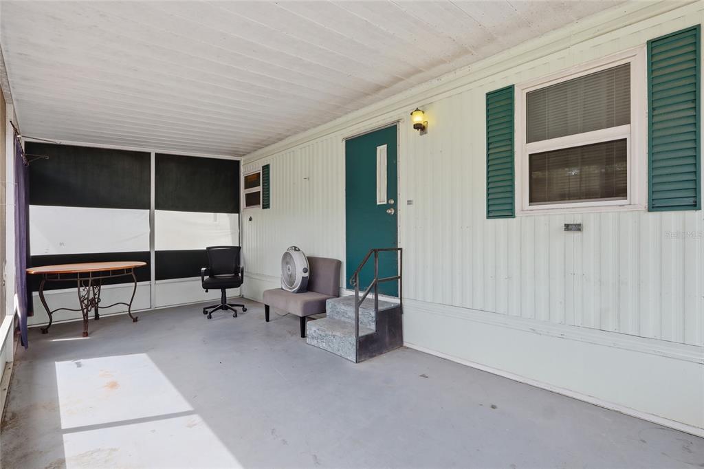 A covered porch features a teal door, gray concrete flooring, and a screened-in seating area — 37622 MARCH LANE, ZEPHYRHILLS, FL
