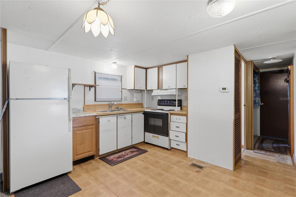 A kitchen features white appliances, wood-toned lower cabinets, white upper cabinets, and light-colored flooring — 37622 MARCH LANE, ZEPHYRHILLS, FL
