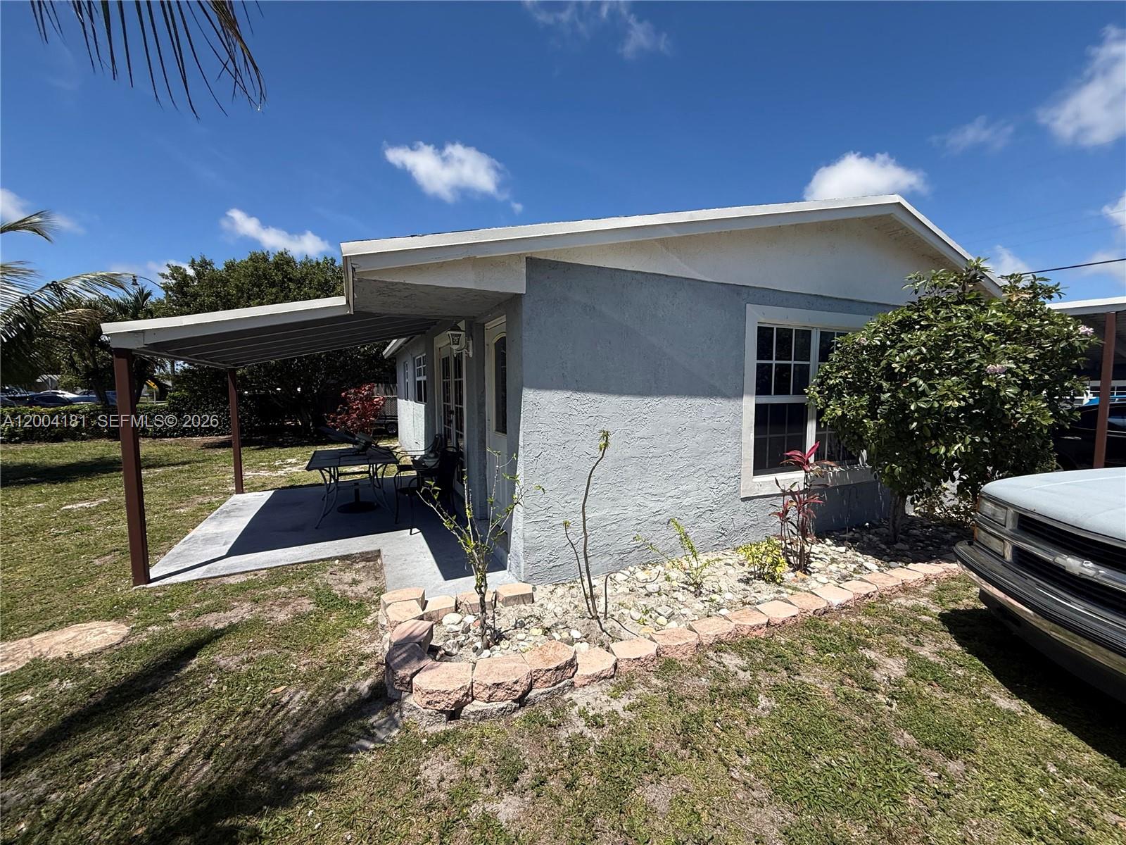 A light gray house features a covered patio and a stone-bordered garden bed — 1701 NW 6th Ave, Pompano Beach FL 33060, POMPANO BEACH, FL