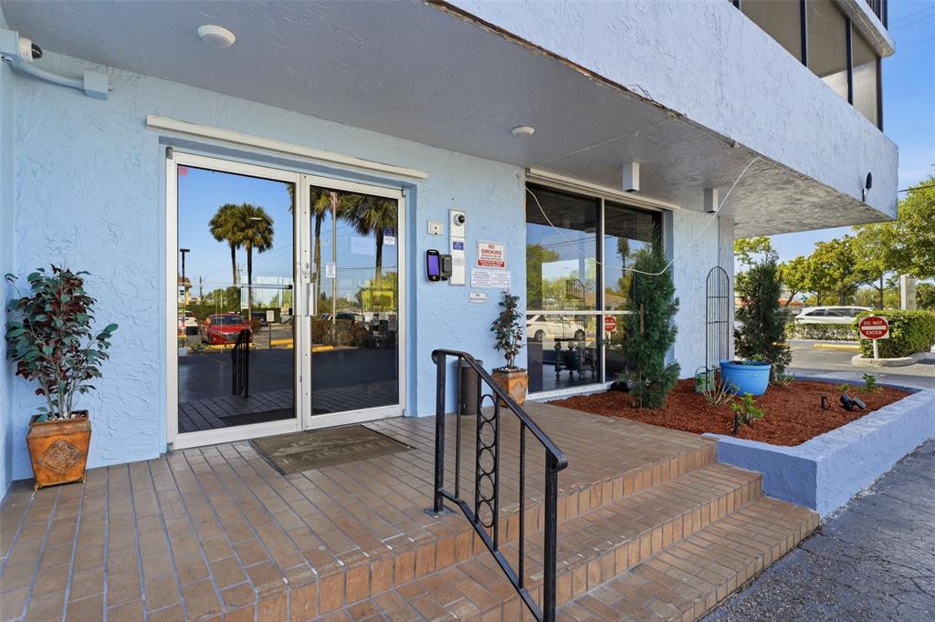 The exterior entrance of a building features blue stucco walls, glass doors, and brick steps — 2901 26TH STREET W UNIT 509, BRADENTON, FL