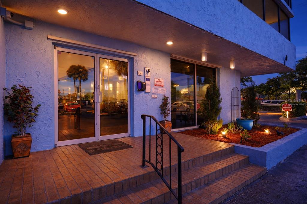 The exterior entrance of a blue building features glass double doors and brick steps — 2901 26TH STREET W UNIT 509, BRADENTON, FL