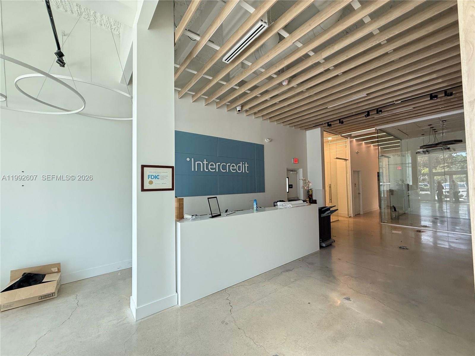 A modern office reception area features a white desk, blue signage, and wood-slat ceiling accents — 10015 NW 41st St # 103, Doral FL 33178, DORAL, FL