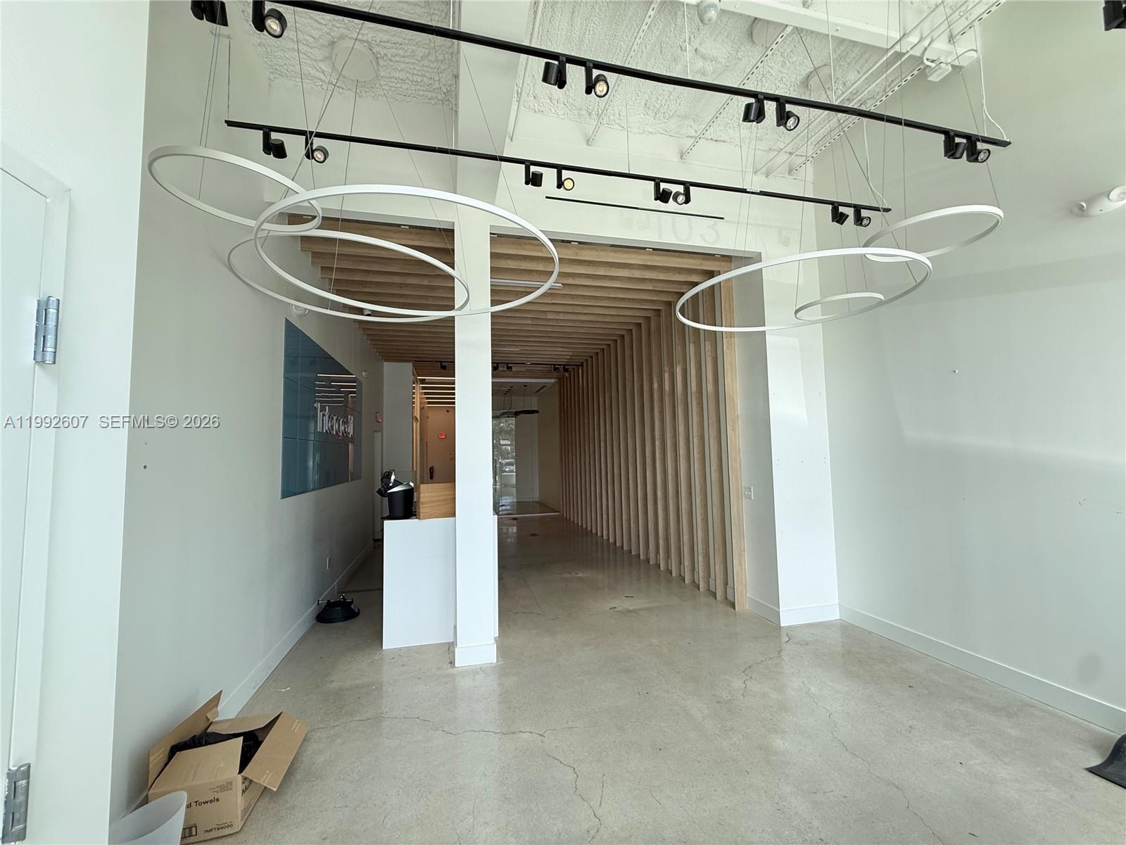 An empty commercial space features concrete floors, track lighting, and a wooden slat ceiling design — 10015 NW 41st St # 103, Doral FL 33178, DORAL, FL