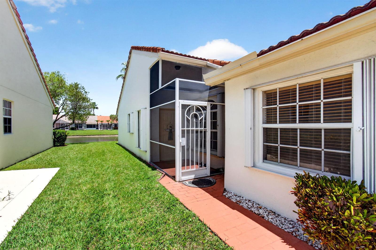 A white house exterior features a screened-in entryway, a red brick path, and a lawn — 6083 Caladium Road, Delray Beach FL 33484, DELRAY BEACH, FL