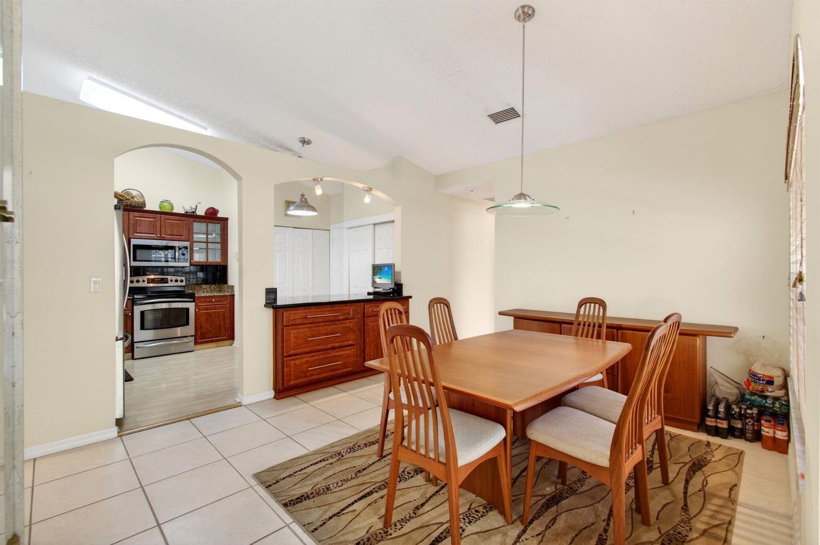 A dining room with a wooden table, chairs, and a kitchen visible through an arched opening — 6083 Caladium Road, Delray Beach FL 33484, DELRAY BEACH, FL