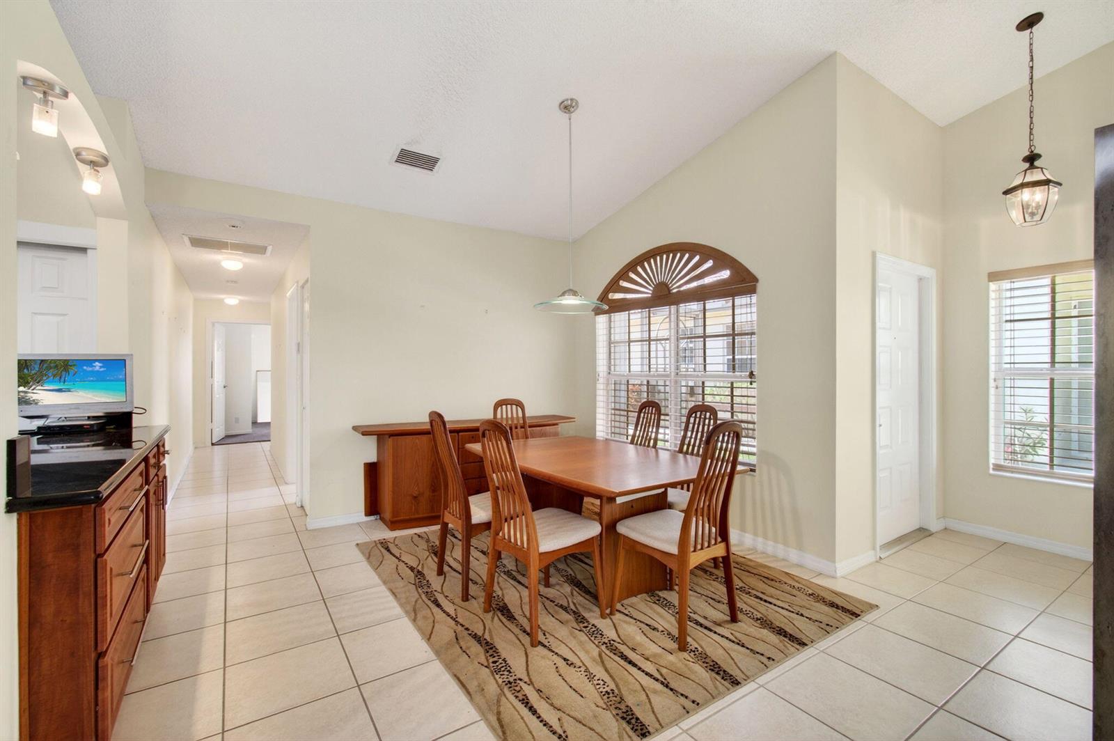 A dining room with a wooden table, chairs, tile flooring, and a large arched window — 6083 Caladium Road, Delray Beach FL 33484, DELRAY BEACH, FL