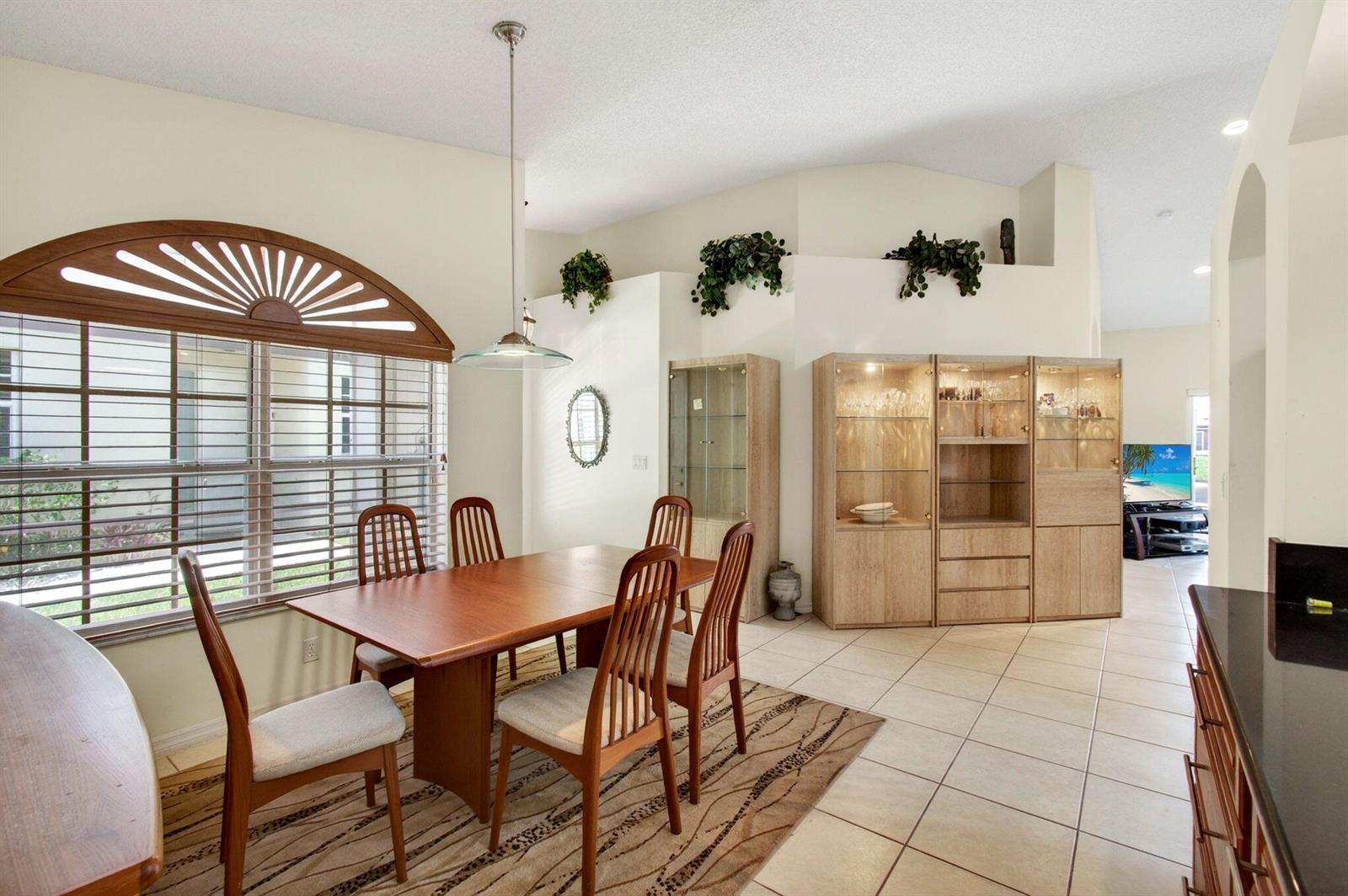 A dining room with a wooden table, chairs, display cabinets, and a large arched window — 6083 Caladium Road, Delray Beach FL 33484, DELRAY BEACH, FL