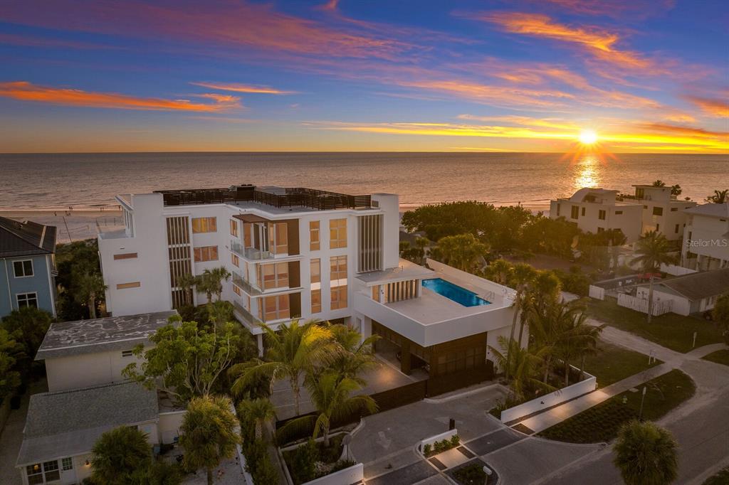 An aerial view of a modern multi-story beachfront home with a rooftop pool at sunset — 84 AVENIDA VENECCIA UNIT 202 & 203, SARASOTA, FL