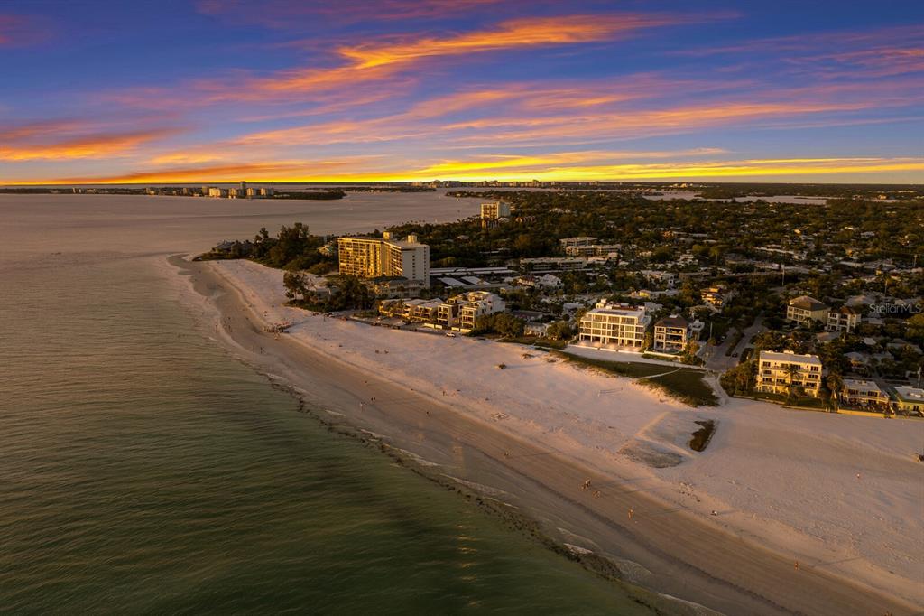 An aerial view of a sandy beach coastline with multi-story buildings at sunset — 84 AVENIDA VENECCIA UNIT 202 & 203, SARASOTA, FL